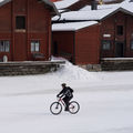 A cyclist cycling past old wooden houses in winter.