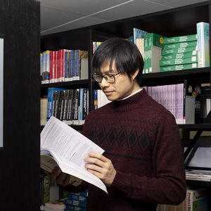 A young man is browsing a book next to a bookshelf in a library.