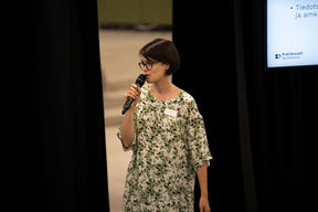 A woman on stage speaks into microphone and looks at the audience.